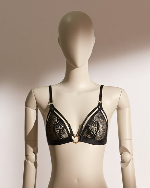 Heartbound Bralette Set in elegant black lace, featuring a wireless bralette with wide supportive straps and a whimsical heart-shaped charm at the center front. Paired with a matching lace thong adorned with fine mesh panels and sleek side straps, this lingerie set blends comfort, playfulness, and refined sensuality from the Pills N Poison collection.