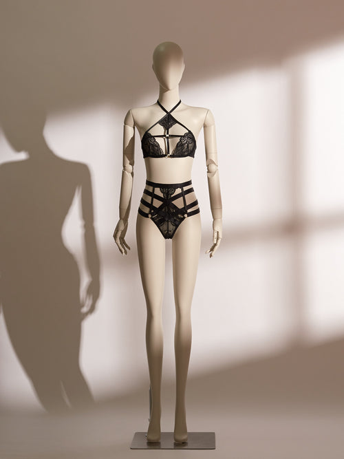 Black lace Isadora Halter Bra Set on mannequin, featuring wide halter straps, underwire bra with front clasp, high-waisted thong with strappy harness design and gold-tone hardware, styled for seductive elegance.