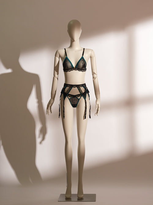 Three-piece emerald and black lace lingerie set featuring a wireless bralette with front closure, matching lace thong, and adjustable garter belt with tassel accents, designed for seductive elegance and confident styling.