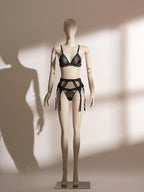 Three-piece Nocturne lingerie set featuring a black sheer mesh bralette with emerald satin trim, matching low-rise thong, and a coordinating high-waisted garter belt with intricate tassel detailing, black lace overlays, and multiple adjustable suspenders. A luxurious and seductive ensemble from Pills N Poison designed to evoke elegance and bold sensuality.