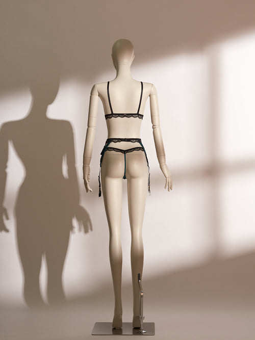 Three-piece Nocturne lingerie set featuring a black sheer mesh bralette with emerald satin trim, matching low-rise thong, and a coordinating high-waisted garter belt with intricate tassel detailing, black lace overlays, and multiple adjustable suspenders. A luxurious and seductive ensemble from Pills N Poison designed to evoke elegance and bold sensuality.